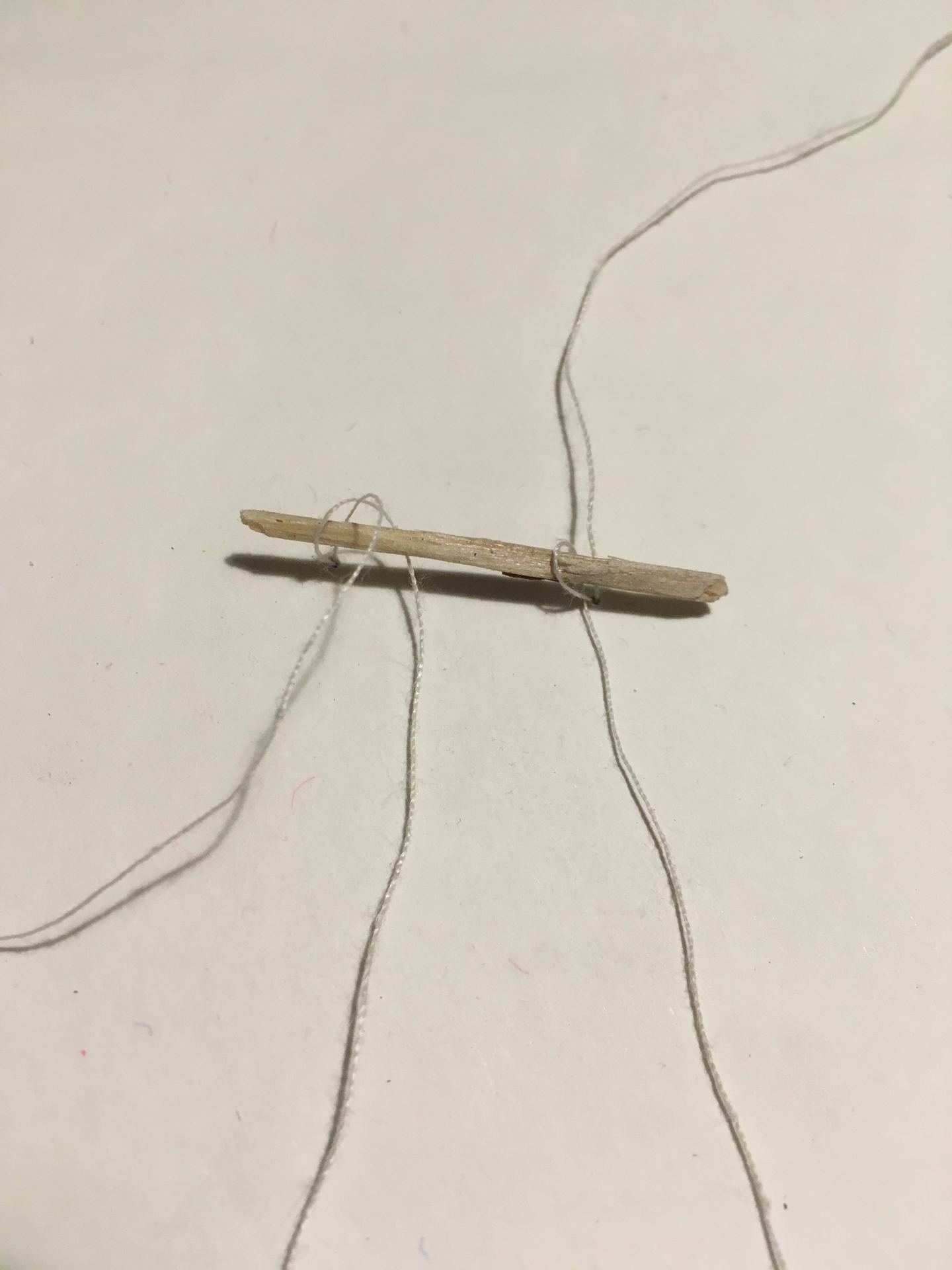 A stick smaller than a match or a toothpick holds the yarn behind the paper.