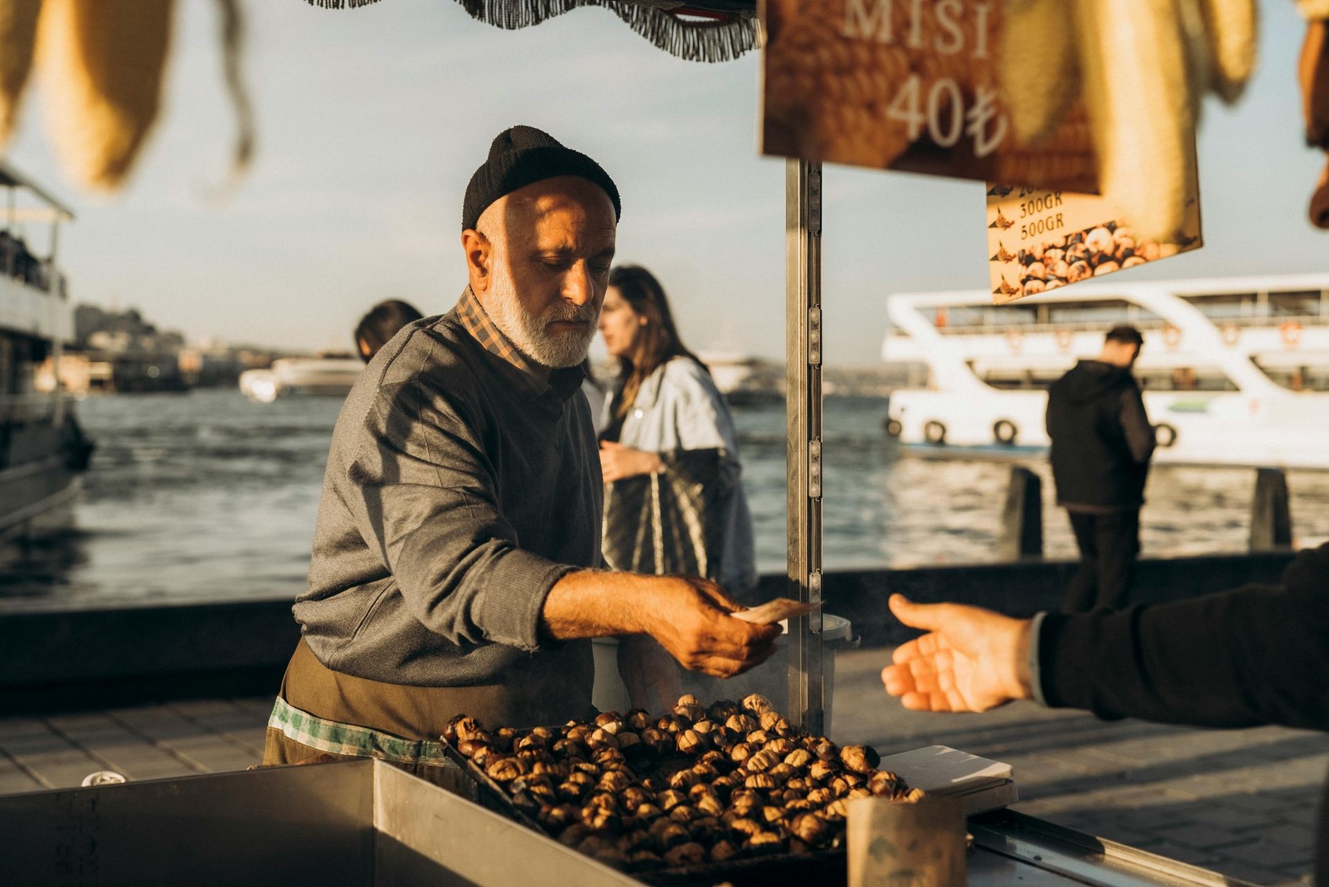 A man selling food at a market near the water