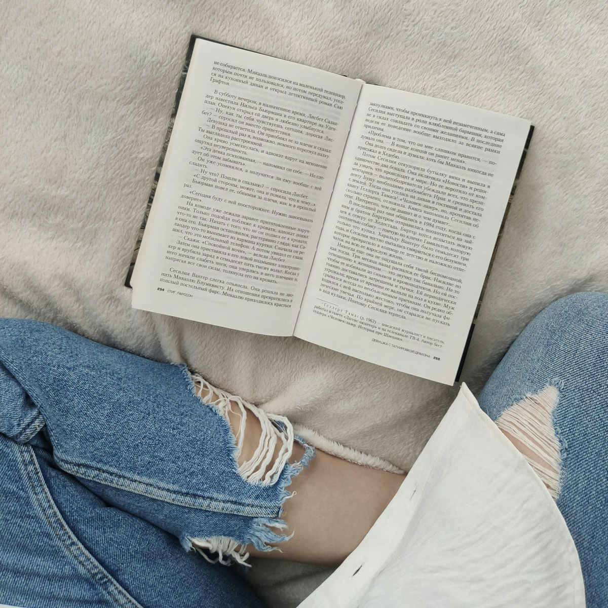 Top view crop anonymous female wearing casual outfit sitting on comfortable soft bed with legs crossed and reading good book in free time