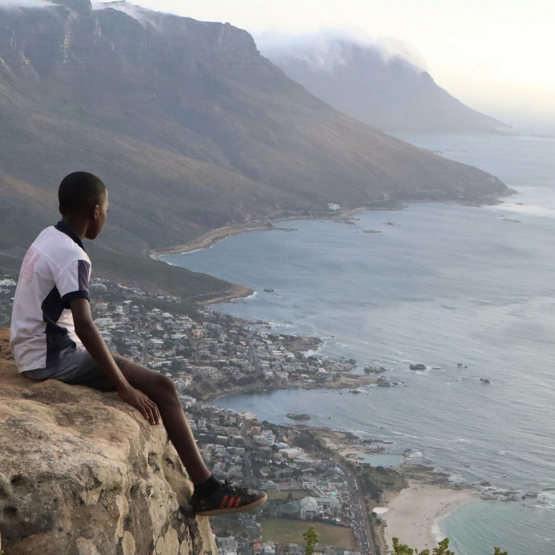 A young boy sits on a rock overlooking the ocean