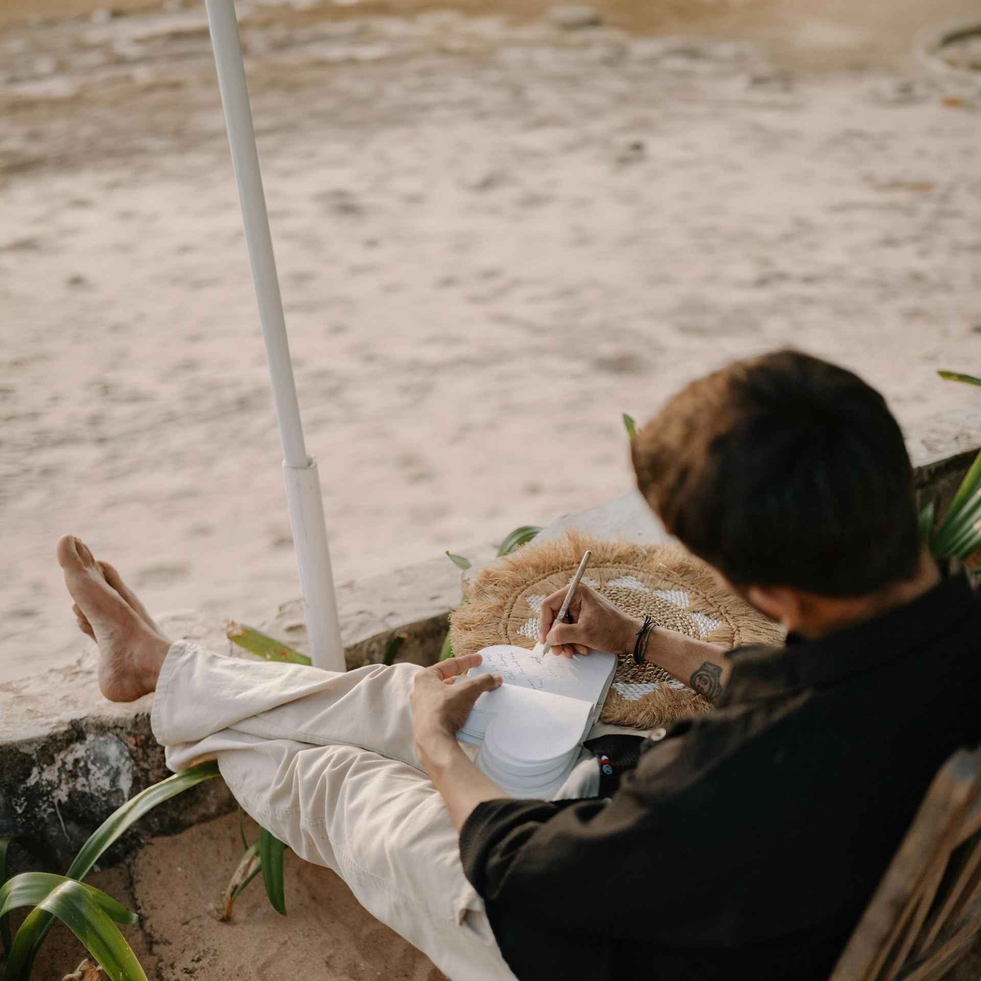 Man relaxing and writing in a journal on a serene beach in Goa, India.