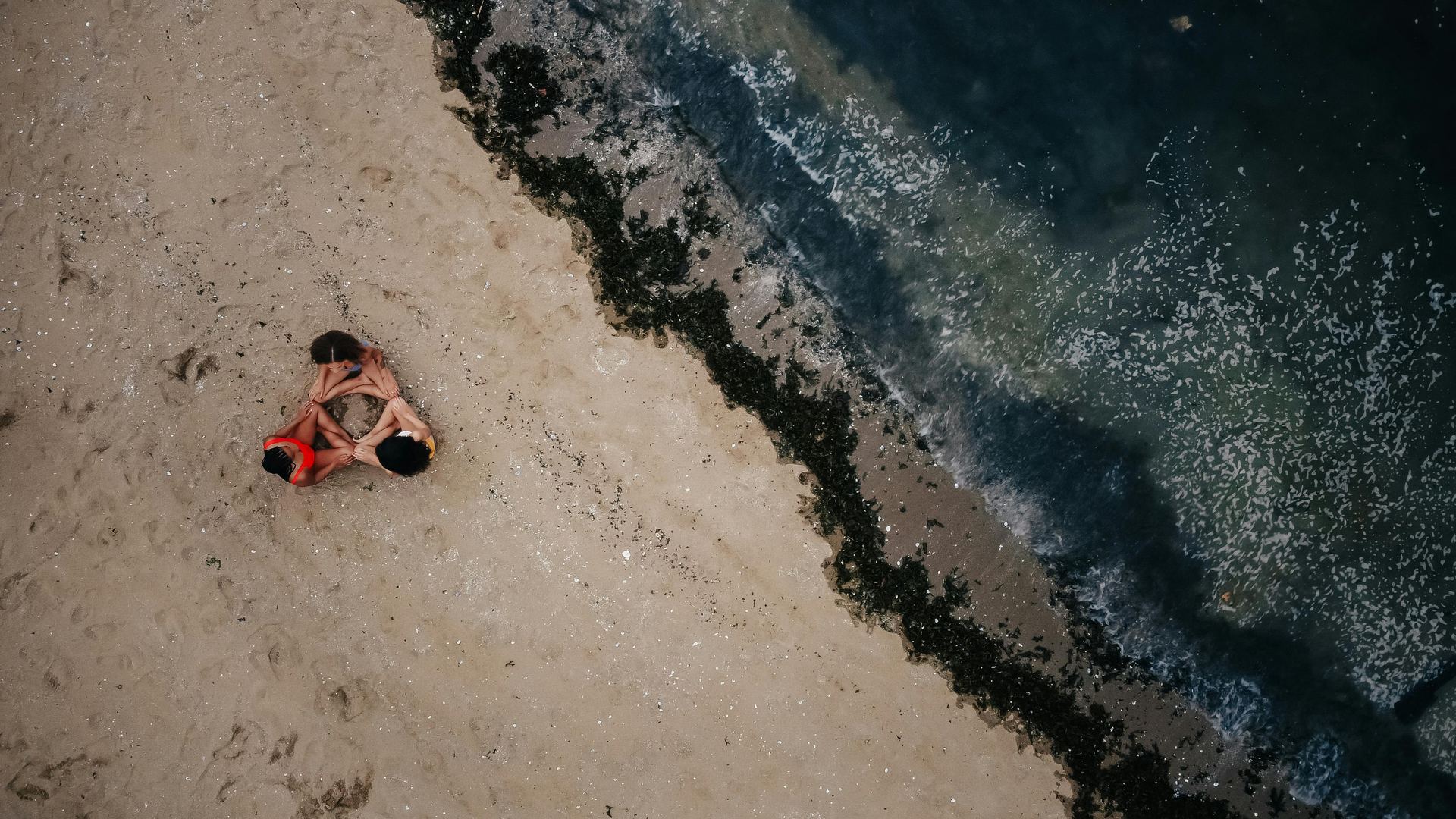 Drone shot capturing three individuals meditating on the sandy shores of Vancouver's beach.