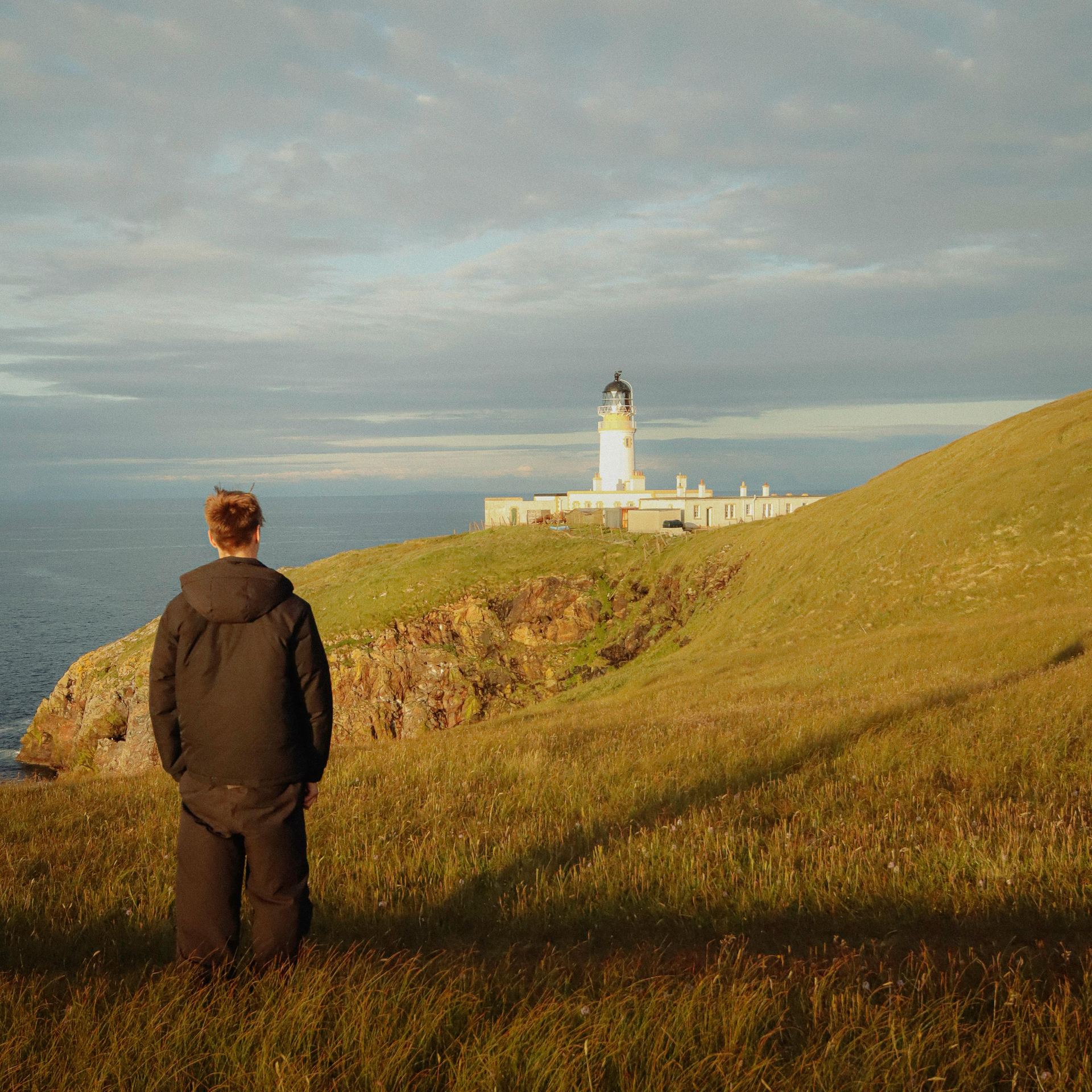 A man standing on a hill looking at a lighthouse