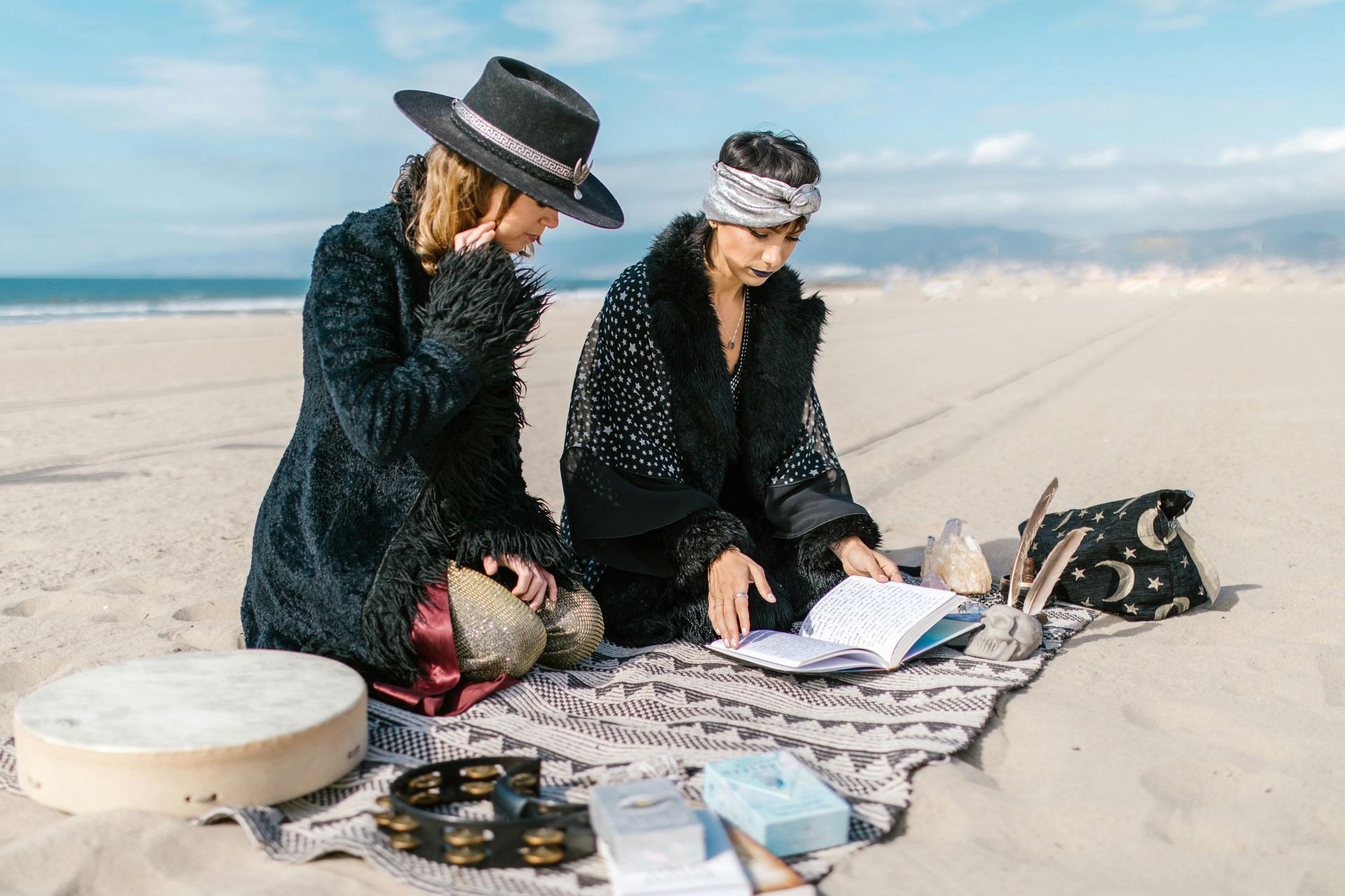 Woman in Black and White Coat Sitting on White Textile on Beach