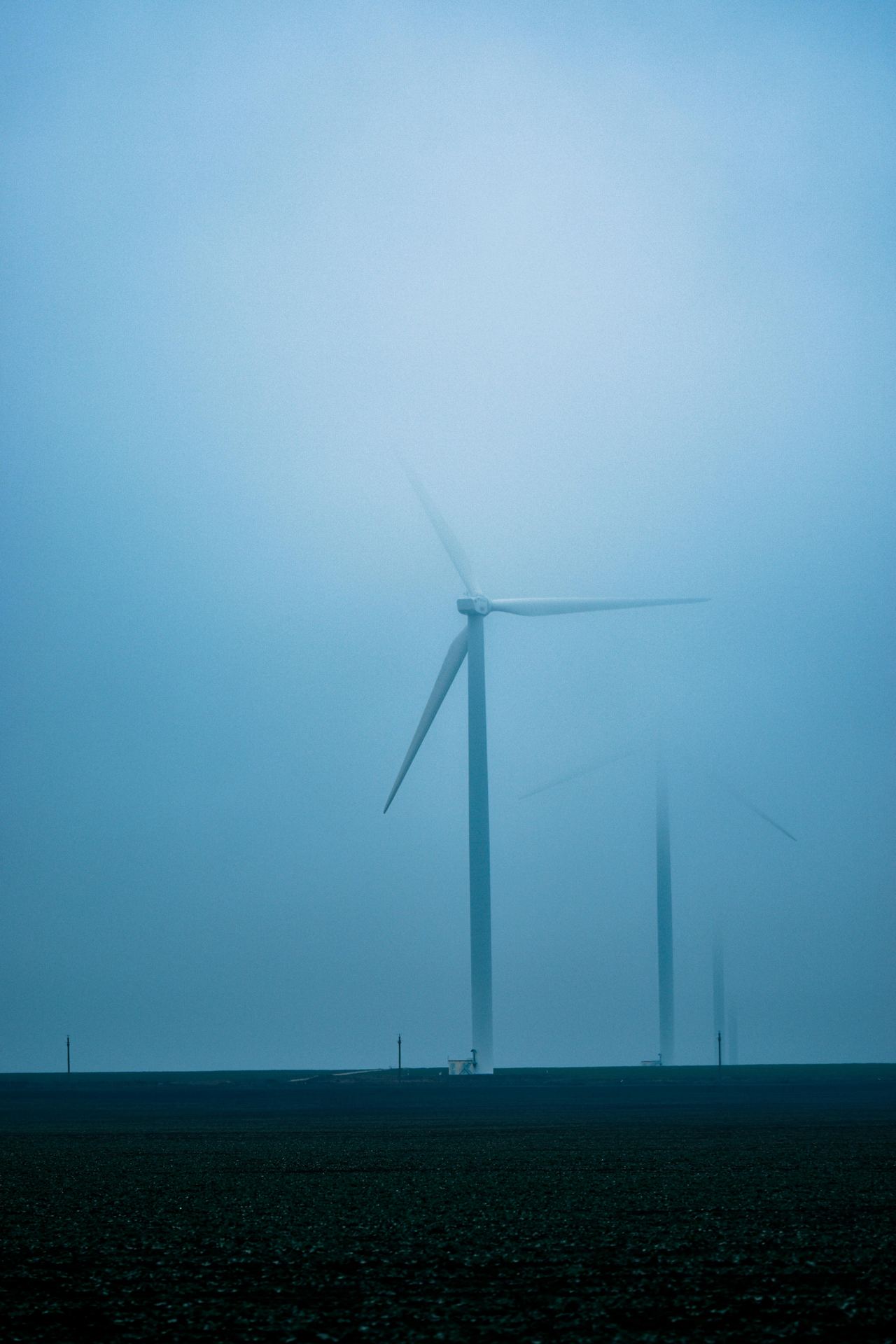 High modern offshore windmills placed in field in countryside under cloudy sky in foggy day