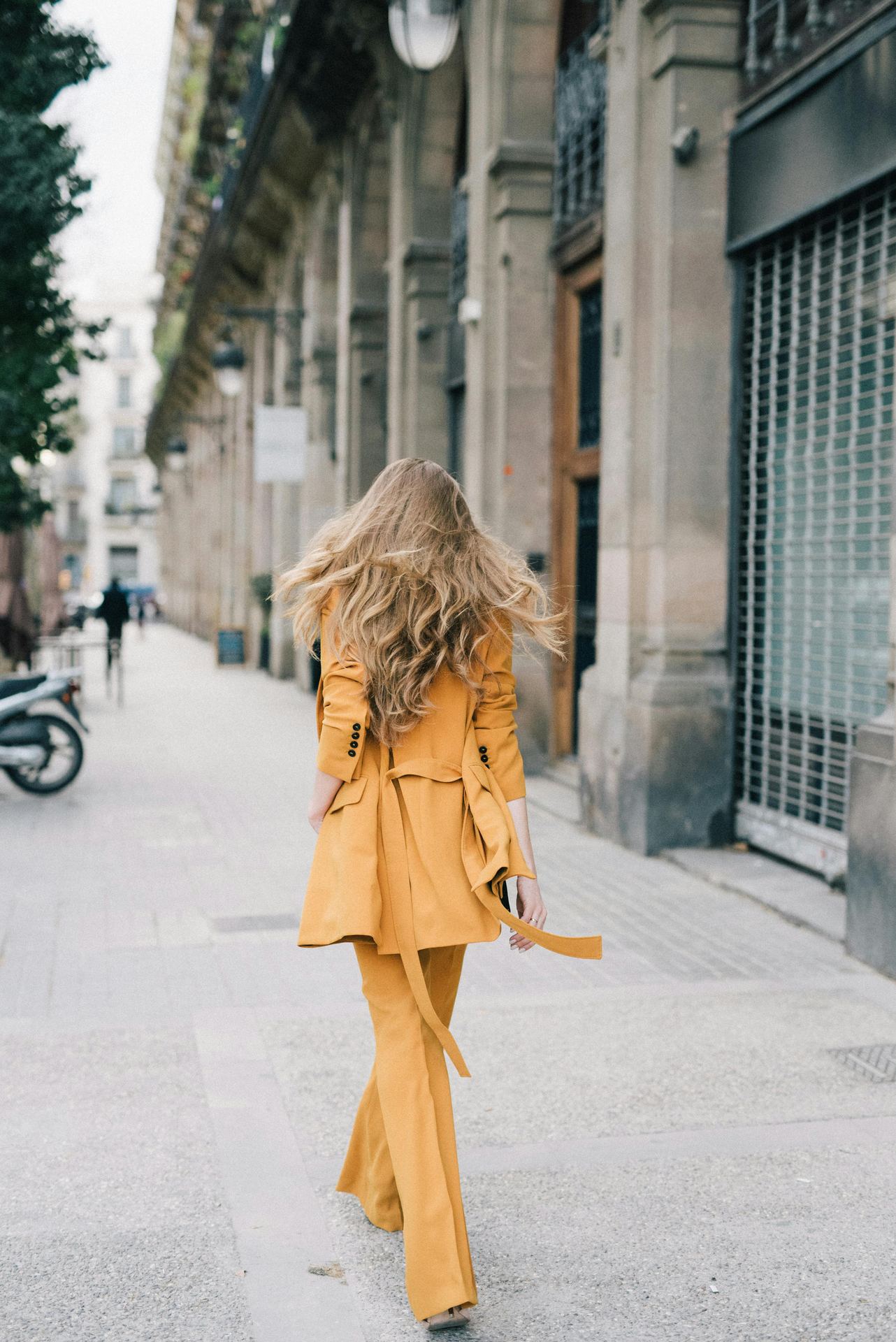 Fashionable woman in a yellow coat walking down a city street, showcasing urban style and elegance.