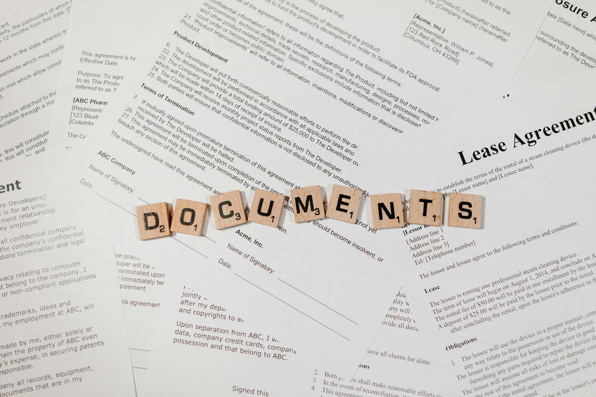 Top view of scrabble tiles spelling 'DOCUMENTS' on various contracts and agreements.